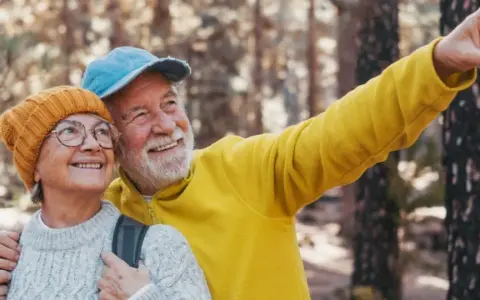 Uśmiechnięta para seniorów w górach, mężczyzna wskazuje palcem.