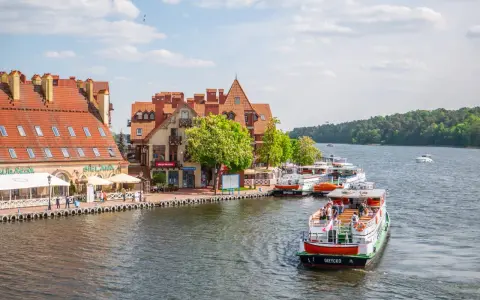 Port w Mikołajkach z zacumowanymi statkami wycieczkowymi i budynkami z czerwonymi dachami. Wspaniałe atrakcje w Mikołajkach czekają na turystów.