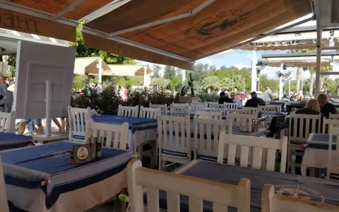 Stoliki w restauracji z niebiesko-białymi obrusami i białymi krzesłami, pod markizą.
