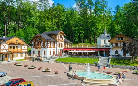 Plac Dietla w Szczawnicy z fontanną, budynkami uzdrowiskowymi i lasem w tle.