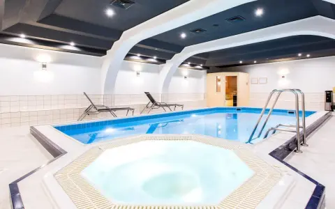 Wnętrze hotelowe z basenem, jacuzzi, sauną i leżakami.