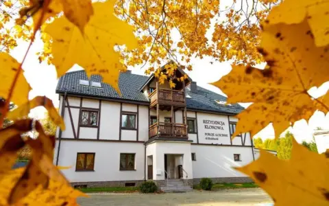 Dom z drewnianymi elementami i balkonem, otoczony jesiennymi liśćmi.