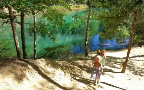 Dwie dziewczynki w słomkowych kapeluszach idą ścieżką nad turkusowym jeziorem.