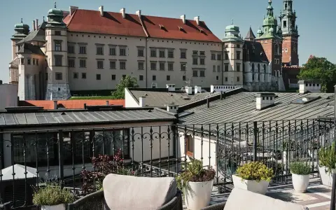 Widok z tarasu na Wawel, z meblami wypoczynkowymi i roślinami w donicach.