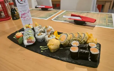 Talerz sushi z różnymi rolkami, w tym smażonymi i z łososiem, na czarnej desce.