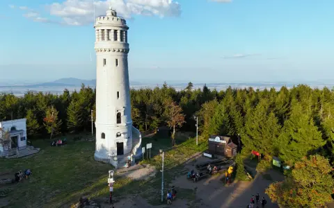 Kamienna wieża widokowa na szczycie góry otoczona lasem, z widokiem na krajobraz.
