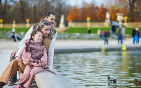 Rodzina z dzieckiem siedzi nad brzegiem stawu z kaczkami w parku.