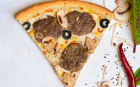 Kawałek pizzy z mięsem mielonym, pieczarkami i oliwkami na jasnym tle.