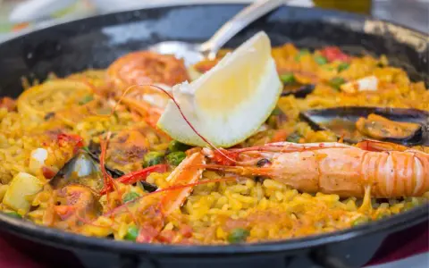 Paella z owocami morza i cytryną w czarnej patelni.
