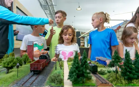 Dzieci oglądają makietę kolejową z pociągami i budynkami.