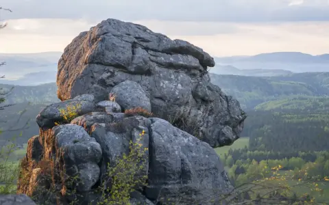 Skaliste formacje w Górach Stołowych z widokiem na zielone wzgórza i lasy.
