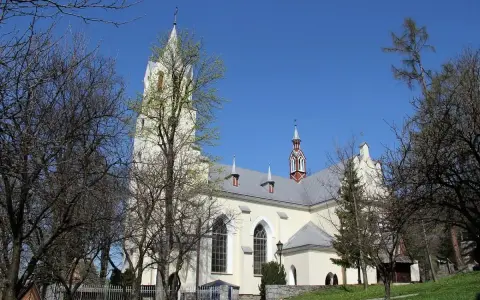 Jasny kościół św. Wojciecha w Szczawnicy z wieżą, otoczony drzewami.