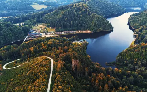 Widok z lotu ptaka na jezioro Bystrzyckie otoczone lasami, z krętą drogą i zabudowaniami.
