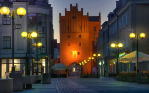 Brama miejska w Olsztynie o zmierzchu, oświetlona latarniami i iluminacją.