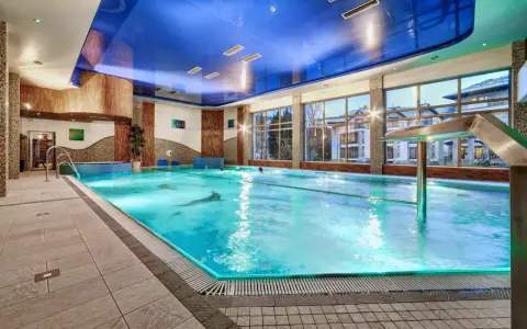Basen hotelowy z niebieskim sufitem i dużymi oknami, woda w basenie jest turkusowa.