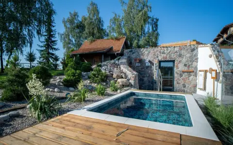 Mały basen z drewnianym tarasem obok kamiennego budynku spa z sauną.