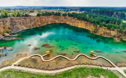 Turkusowe jezioro w kamieniołomie z drewnianą kładką i altaną.