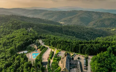 Widok z lotu ptaka na hotel SPA z basenem i zjeżdżalnią, otoczony lasem i górami.