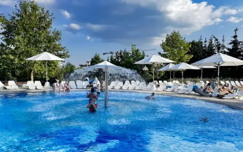 Rodzinna zabawa w hotelu z basenem na Mazurach. Dzieci pluskają się w wodzie, dorośli odpoczywają na leżakach pod białymi parasolami.