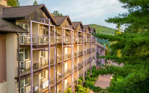 Hotel z balkonami w otoczeniu zieleni i gór.