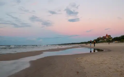 Plaża w Łebie o zachodzie słońca z widokiem na morze i budynek z czerwonym dachem.