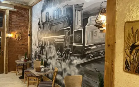 Wnętrze restauracji z muralem przedstawiającym lokomotywę i stoliki.