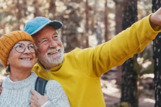 Uśmiechnięta para seniorów w górach, mężczyzna wskazuje palcem.