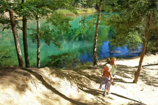 Dwie dziewczynki w słomkowych kapeluszach idą ścieżką nad turkusowym jeziorem.