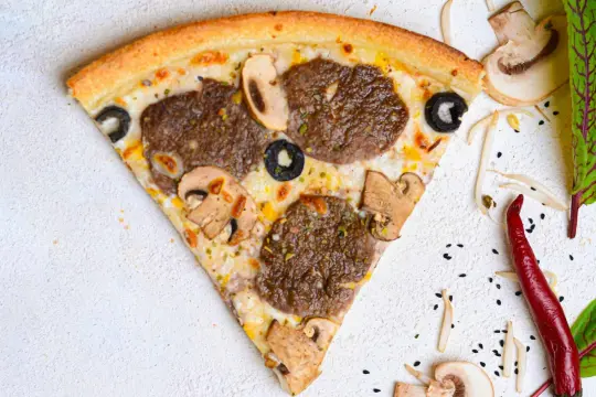 Kawałek pizzy z mięsem mielonym, pieczarkami i oliwkami na jasnym tle.