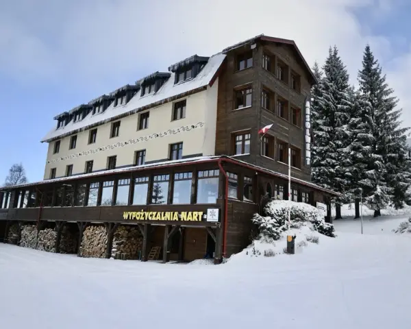 Hotel w Zieleńcu zimą, z widoczną wypożyczalnią nart i stosem drewna.