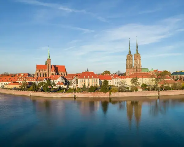Widok na Ostrów Tumski we Wrocławiu z rzeką i odbiciem budynków w wodzie.