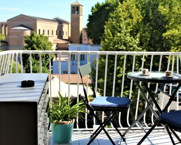 Balkon z widokiem na rzymskie budynki i zieleń, stolik z kawą.
