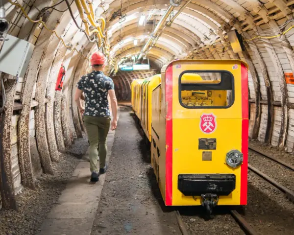 Mężczyzna w kasku idzie obok żółtej kolejki górniczej w tunelu kopalni.