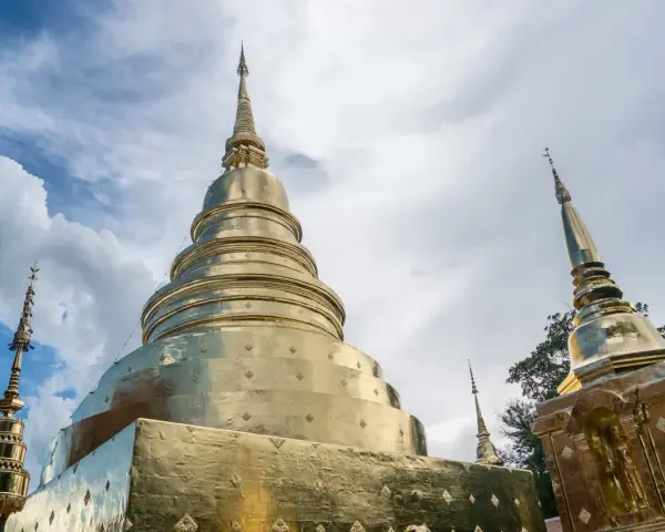 Złote stupy świątyni Wat Phra Singh w Chiang Mai na tle błękitnego nieba z chmurami.