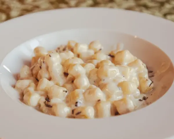 Kluski gnocchi w kremowym sosie z tartą truflą na białym talerzu.
