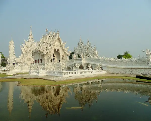 Biała świątynia Wat Rong Khun w Tajlandii z odbiciem w stawie.