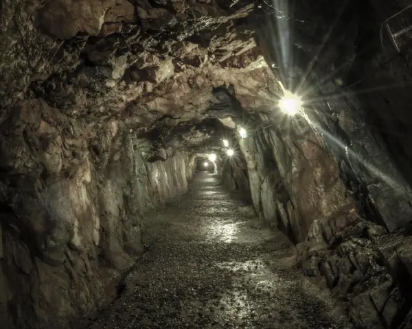 Wydrążony tunel skalny z oświetleniem, kamienista ścieżka.