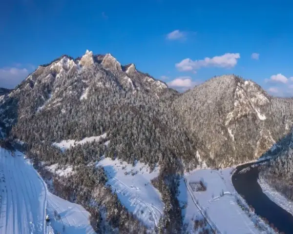 Zimowe Trzy Korony pokryte śniegiem, z lasem i rzeką w dolinie.