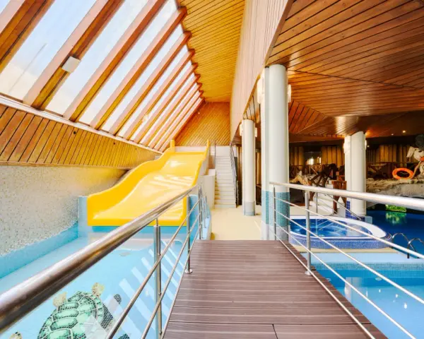 Wnętrze hotelowe z basenem, zjeżdżalnią i jacuzzi, drewniany sufit i ściany.