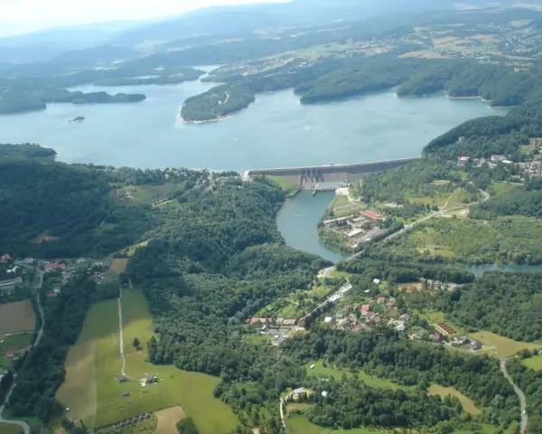 Widok z lotu ptaka na zalesione wzgórza, jezioro i zaporę wodną.