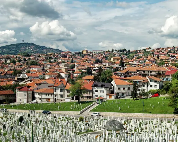 Widok na cmentarz i miasto z dachami z czerwonej dachówki pod zachmurzonym niebem.