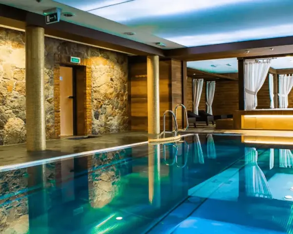 Basen w hotelu SPA z kamienną ścianą i drewnianymi elementami, z zasłonami w tle.