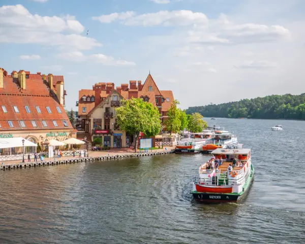 Port w Mikołajkach z zacumowanymi statkami wycieczkowymi i budynkami z czerwonymi dachami. Wspaniałe atrakcje w Mikołajkach czekają na turystów.