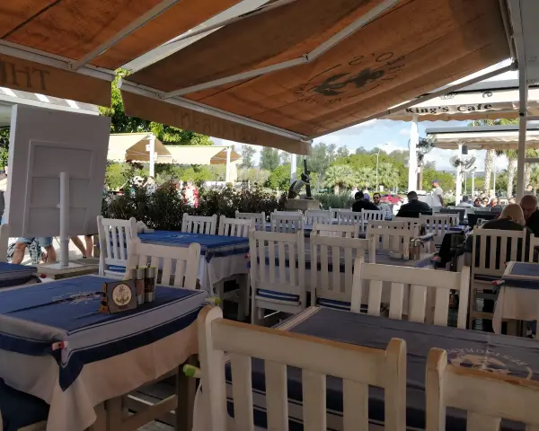 Stoliki w restauracji z niebiesko-białymi obrusami i białymi krzesłami, pod markizą.