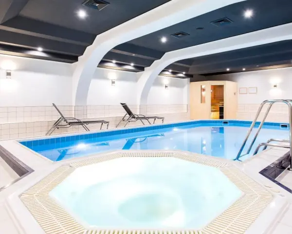 Wnętrze hotelowe z basenem, jacuzzi, sauną i leżakami.