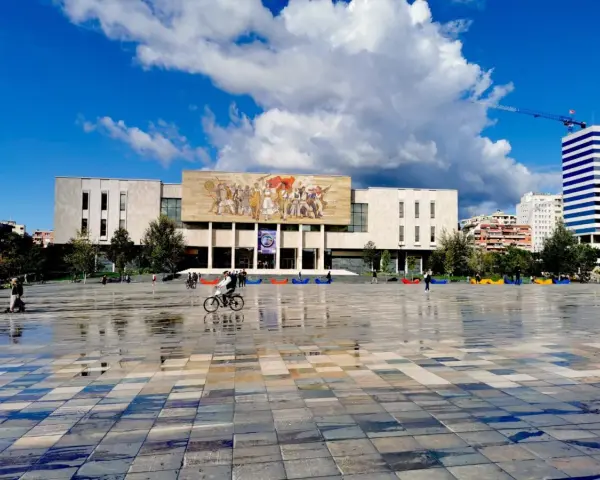 Plac w Tiranie z budynkiem Narodowego Muzeum Historii i kolorowymi pufami.