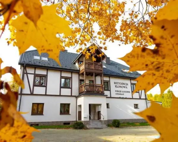 Dom z drewnianymi elementami i balkonem, otoczony jesiennymi liśćmi.