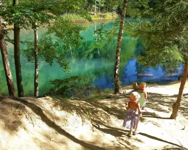 Dwie dziewczynki w słomkowych kapeluszach idą ścieżką nad turkusowym jeziorem.