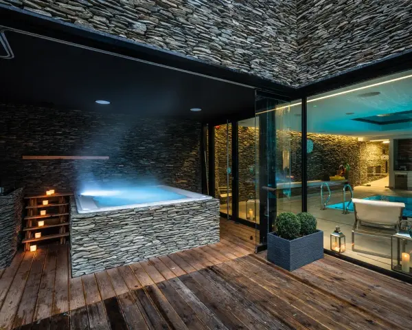 Nowoczesne jacuzzi z kamienną okładziną i oświetleniem, obok basenu.