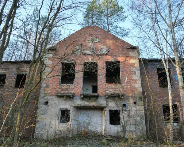 Opuszczony budynek z cegły z pustymi oknami, otoczony drzewami.